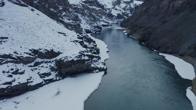 Indus River winds through snow-covered mountains in Leh Valley near Hemis National Park, Ladakh. Aerial view captures the frozen winter landscape with glacial blue water cutting through white terrain.