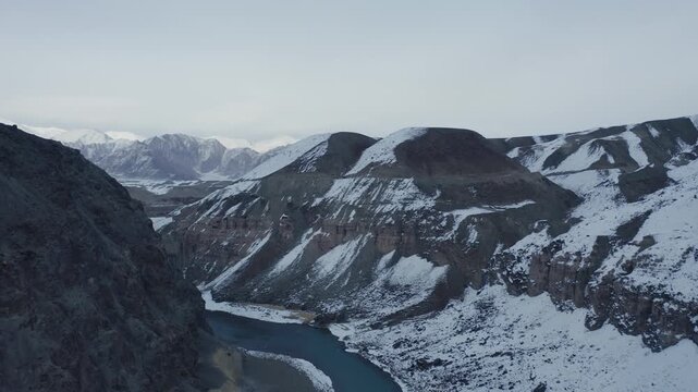 Indus River winds through snow-covered valley surrounded by Himalayan mountain ranges in Ladakh, India during winter season. Smooth forward motion reveals river meandering through ice and snow patches