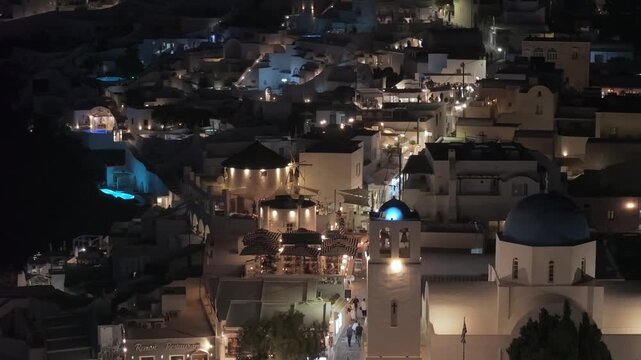 A night view of Fira, Santorini, showcasing the vibrant, illuminated white houses contrasting against the vast, dark mystery of the volcanic caldera and the Aegean Sea.