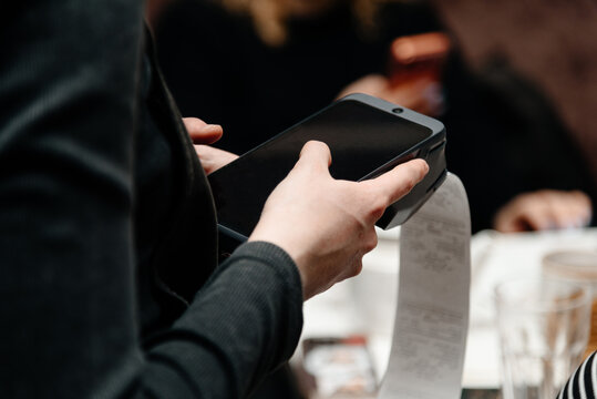 waitress holding in hands electronic cash register for contactless payment with paper receipt in cafe or restaurant, smart terminal