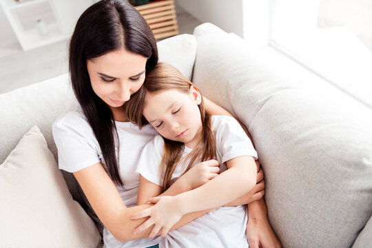 Mother cuddling her sleeping daughter on a sofa at home, family love and comfort during a tender bonding and parenting moment