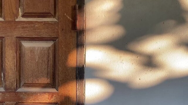 Warm golden sunlight and shadow overlay on a rustic wooden door and concrete wall.