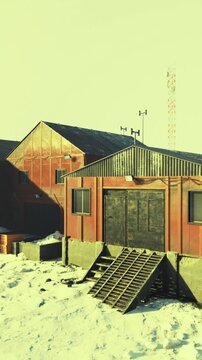 A building stands in a snowy landscape with a set of stairs leading up to the entrance. Equipment is visible on the roof, and the surrounding area looks cold.
