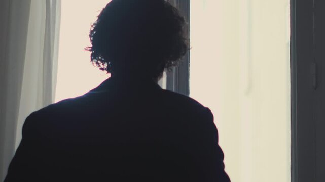Man opening curtain by window letting soft daylight in