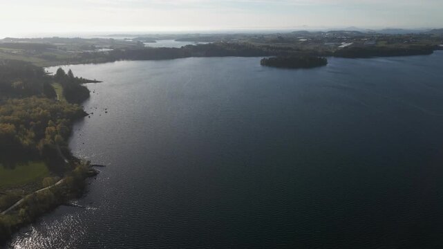 Cinematic 4K aerial drone footage capturing the vast expanse of Store Stokkavannet (Lake Stokkavannet) and its surrounding residential landscape in Stavanger, Rogaland, Norway. The scene features clea