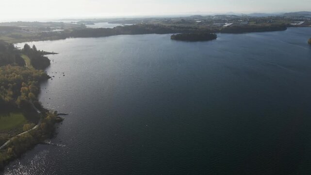 Cinematic 4K aerial drone footage capturing the vast expanse of Store Stokkavannet (Lake Stokkavannet) and its surrounding residential landscape in Stavanger, Rogaland, Norway. The scene features clea