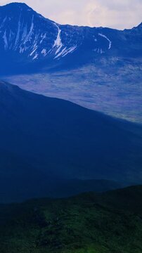 The view shows high mountains with snow on the peaks and green valleys below. The sky is blue with some clouds. This scene appears to be in a remote natural area.