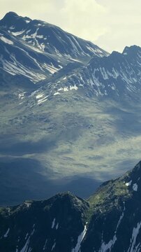 Majestic mountains with snow on their peaks stretch across the horizon. Valleys lie below. Sunlight casts shadows on the rocky terrain. Nature shows its beauty in this landscape.