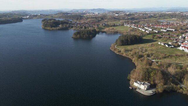 Cinematic 4K aerial drone footage capturing the vast expanse of Store Stokkavannet (Lake Stokkavannet) and its surrounding residential landscape in Stavanger, Rogaland, Norway. The scene features clea