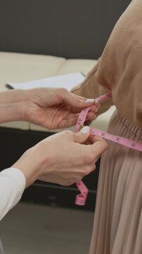 Vertical shot of anonymous nurse using pink measuring tape to measure waist of unrecognisable female patient