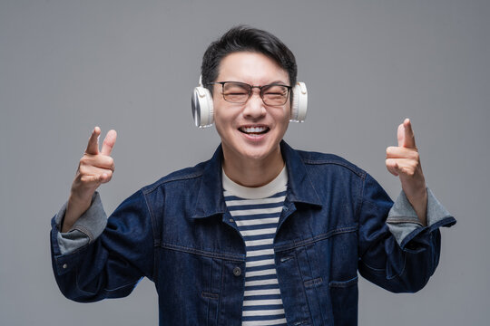 Cheerful Asian man wearing wireless headphones listening to music with eyes closed, happy male enjoying sound or podcast on grey background
