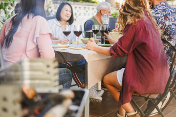 Group of friends having fun at barbecue dinner drinking red wine - Food, friendship, and summer people lifestyle concept - Focus on right girl hand holding glass
