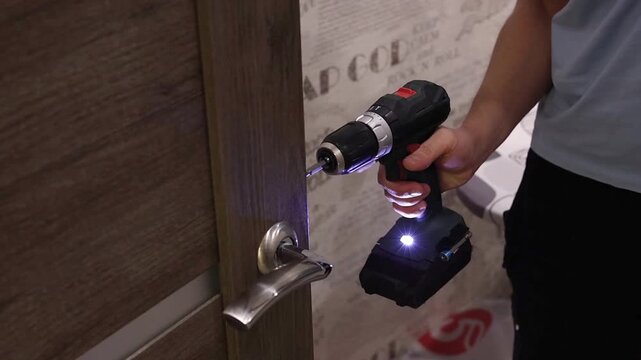Man using cordless drill to remove door handle at home, DIY repair process, home maintenance task, renovation concept.