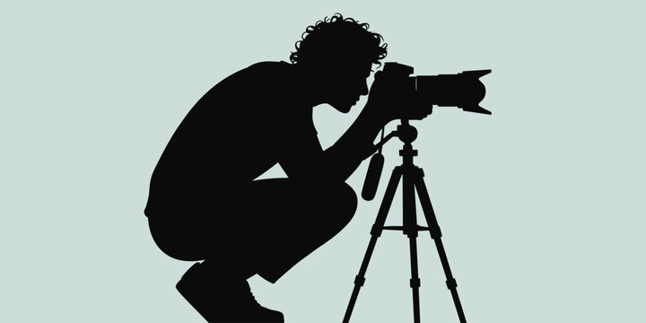 Silhouette of a creative freelance photographer crouching low with a professional DSLR camera mounted on a tripod, capturing a unique angle, possibly for nature, wildlife, event coverage, or street ph