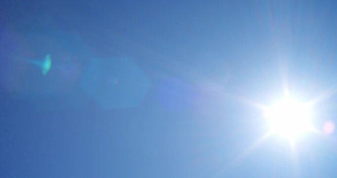 Real-time panning shot of bright sun in a clear blue sky with a sharp natural sunburst effect