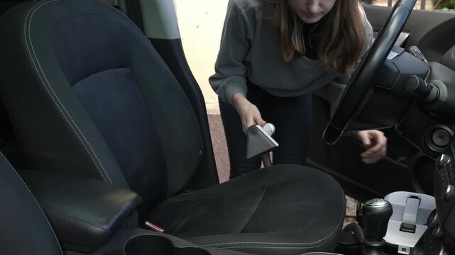 Using a vacuum cleaner to clean car seat upholstery at home in the afternoon