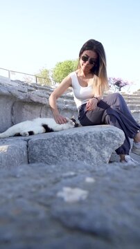Tourist woman petting stray cat in Teos ancient theater Turkey