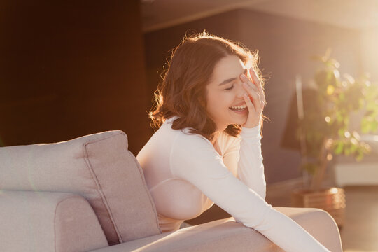 Young woman laughing on a sofa in warm sunlight at home, relaxed and joyful moment in a cozy living room with natural light and casual lifestyle vibe