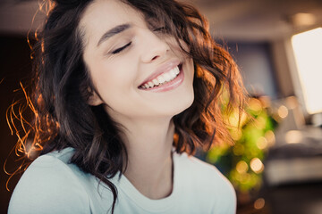 Obraz premium Smiling young woman with closed eyes enjoying a joyful moment in a warm indoor lifestyle portrait