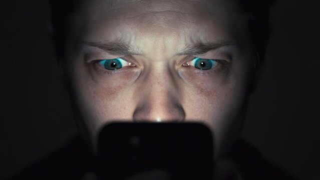 A person's intense gaze illuminated by a smartphone screen, ideal for content focusing on digital interaction, technology usage, and screen-related topics.