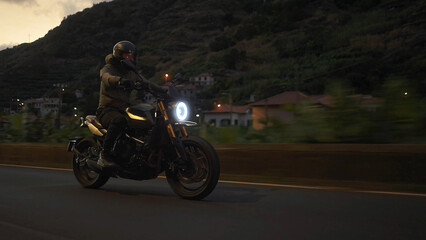 Fototapeta premium Biker riding motorcycle on mountain road during dusk