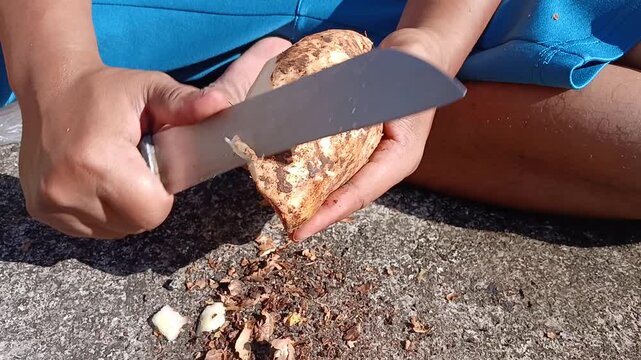 Man Peeling Yam with Knife Outdoors
