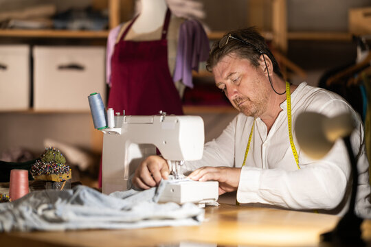 Man seamstress operating by sewing machine, manufactures clothing