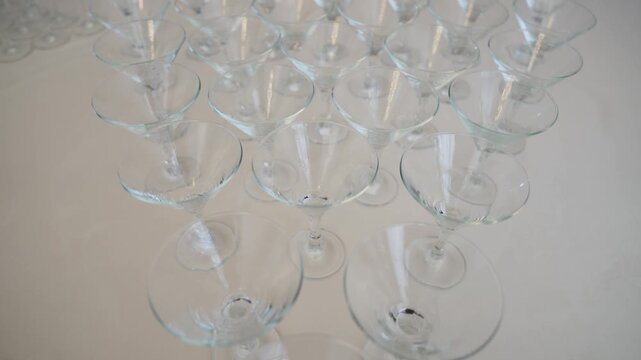 Camera moves over a pyramid of empty martini glasses arranged on a white table. Elegant setup for a wedding, party, or celebration. Clean, sophisticated, and ready for drinks