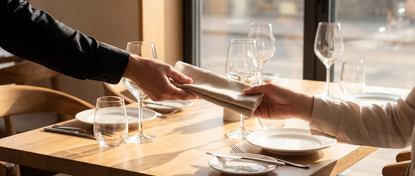 waiter handing napkin guest elegant restaurant together professional service hands bond care hospitality fine dining connection luxury interior formal meal table white cloth attentive