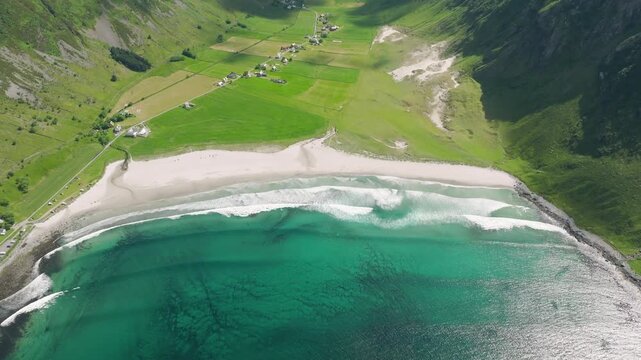 Cinematic aerial view of scenic Norwegian fjord and white sand beach in summer. Crystal clear turquoise water and rocky mountains landscape in Norway. Stunning arctic nature from drone perspective.