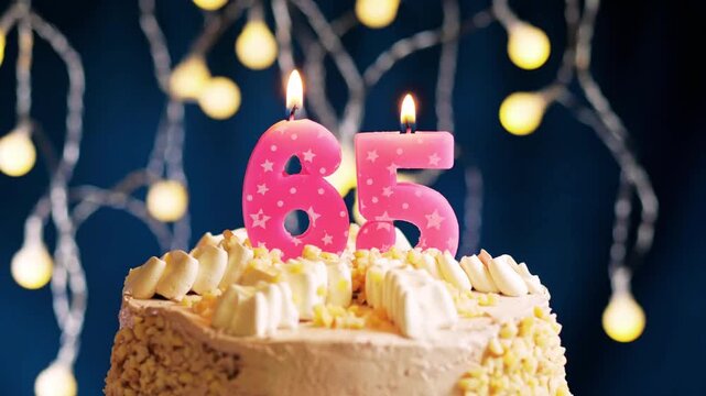 Slow motion close-up of a birthday cake with pink number 65 candle being blown out on a blue background, capturing a joyful milestone birthday celebration moment.