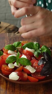 Vertical video. Preparation of caprese salad. Adding spices to caprese salad made of tomatoes, mozzarella and basil.