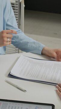 Vertical shot of anonymous healthcare worker giving gentle handshake to unknown patient over desk with medical documents and digital tablet in IVF clinic