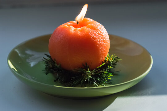 Burning candle in the shape of a tangerine on a green plate