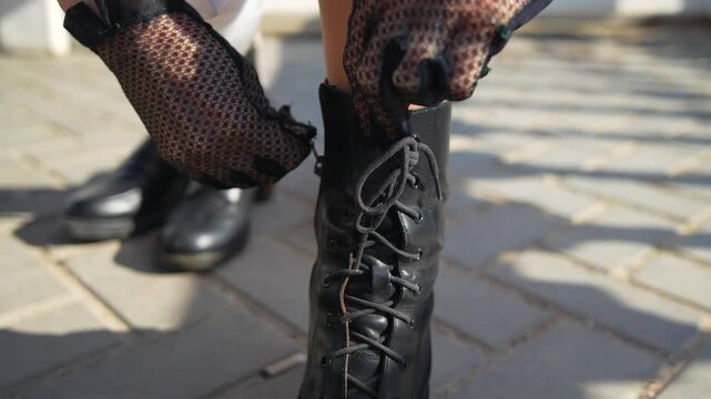 Boots Laces Footwear woman wearing fishnet gloves zips up black leather combat boots while standing on a paved outdoor path