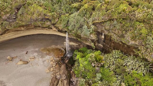 Waterfall cascading from cliff directly on Punakaiki beach, Truman Track in New Zealand. Aerial top-down view