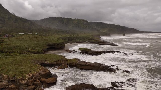 Dramatic and wild rocky coastline with waves crashing on moody, overcast day on Truman Track, New Zealand. Aerial drone panoramic view