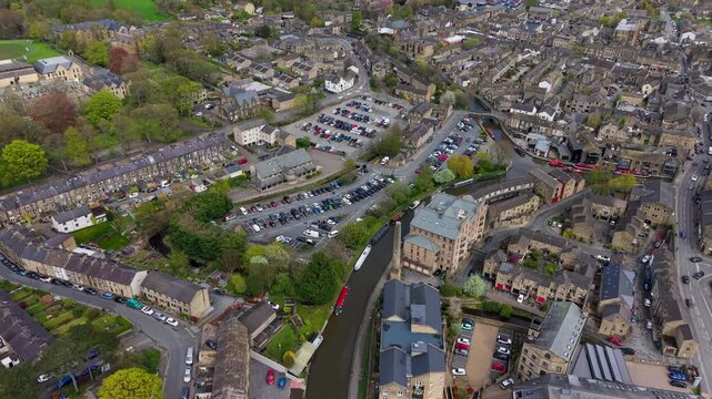 A drone tracks the Leeds and Liverpool Canal into Skipton's historic canal basin, revealing red pleasure cruise boats, a narrowboat, and the surrounding town centre. North Yorkshire, spring.