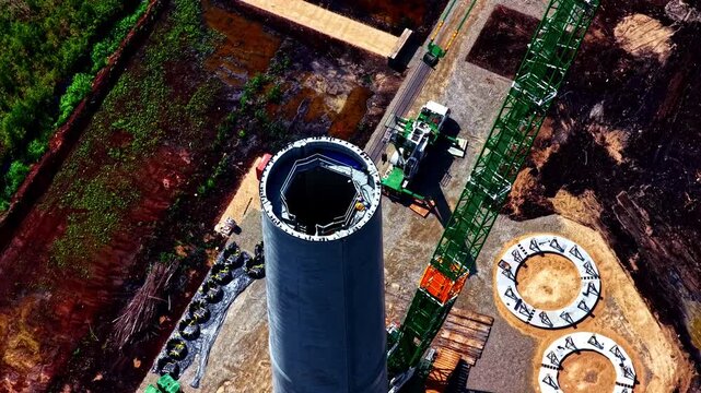 Top down aerial view of a wind turbine tower under assembly with crane and internal structure visible. Detailed look at construction process and engineering of renewable energy infrastructure.
