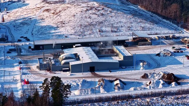 Drone view of industrial energy facility in snowy landscape. Plant with buildings and emissions showing power generation, waste processing or heating system in cold environment.