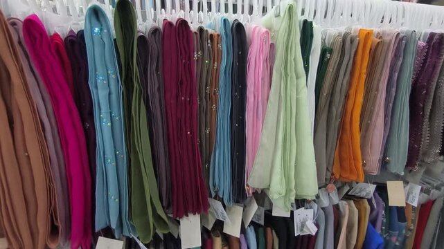 Colorful square hijabs hang neatly on display hangers. These popular headscarves are ready for sale. They are a high-demand fashion choice for Muslim women.