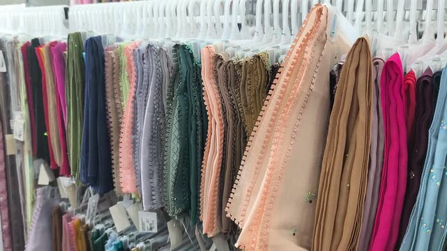 Colorful square hijabs hang neatly on display hangers. These popular headscarves are ready for sale. They are a high-demand fashion choice for Muslim women.
