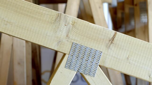 Close up of metal connector plate fixing wooden roof beams in construction. Structural detail showing timber framing and reinforcement in building process.