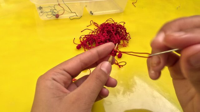 Close-up of Moroccan artisan making Aqad knots by hand using a hook tool. Traditional textile technique creating decorative buttons for caftans and djellabas, showcasing craftsmanship.