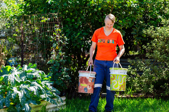 Australian woman in backyard garden carrying buckets for food scraps to compost