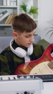 Handsome teenager blogger recording video class tutorial to play guitar on modern smartphone at home studio. Teen boy showing how play for electric guitar for internet auditory. Slow motion
