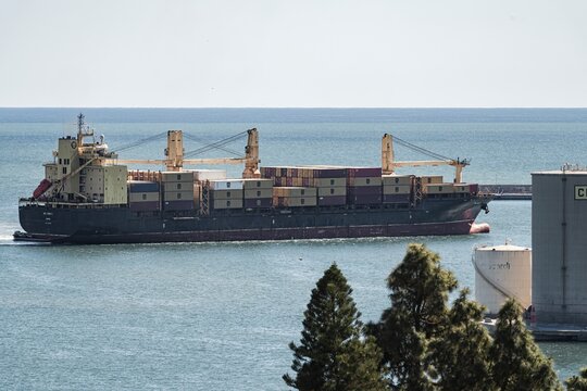 Malaga, Spain; March 29, 2026: A cargo ship full of containers sails through the port and is seen from the mountain; at the back of the ship we can see the small emergency boat to be used in case of s