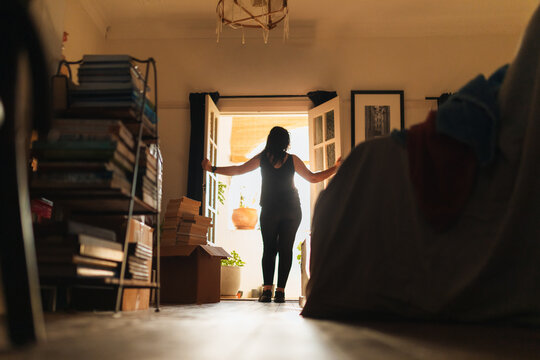 Woman standing in doorway, opening doors to bright sunlight and plants