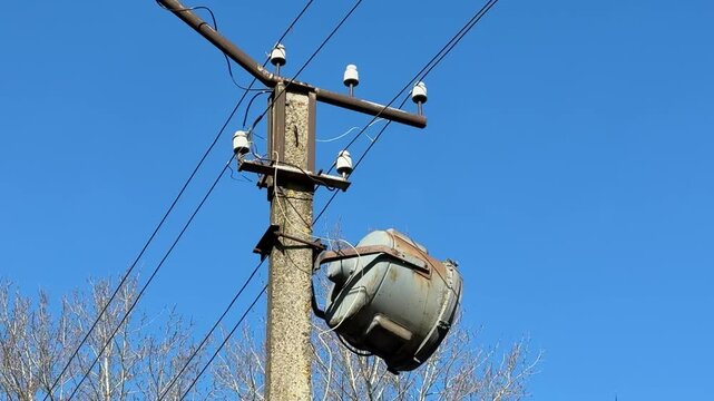 Spotlight on concrete pole, blue sky. Side view of large industrial light fixture hanging from utility pole, power wires crossing