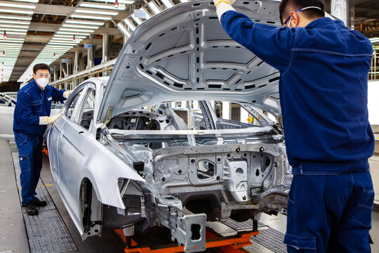 Two Asian workers are working on a car production line.